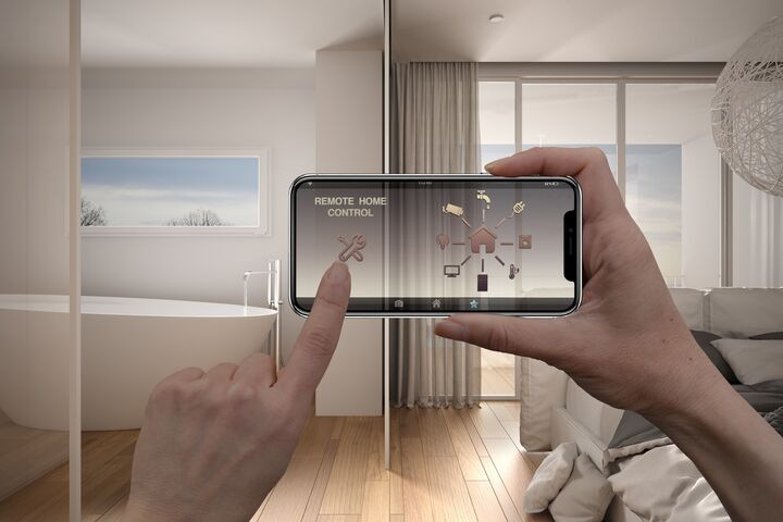 Hände, die ein Handy mit einer geöffneten App vor das Badezimmer und Schlafzimmer halten.