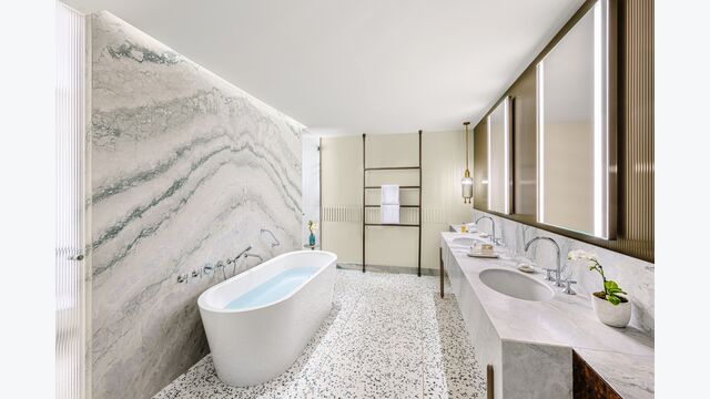 Badezimmer mit Marmor-Wand, davor eine freistehende weiße Badewanne.