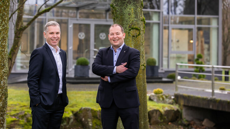 © Kludi GmbH & Co. KG Die Kludi Geschäftsleiter Florian Schindler und Axel Stoiber vor einem Gebäude im Grünen.