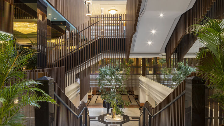 © Melia Hotels International Blick in die Lobby aus der Perspekte des Stiegenaufganges. Hölzerne Elemente und Pflanzen schaffen eine einladende Atmosphäre.