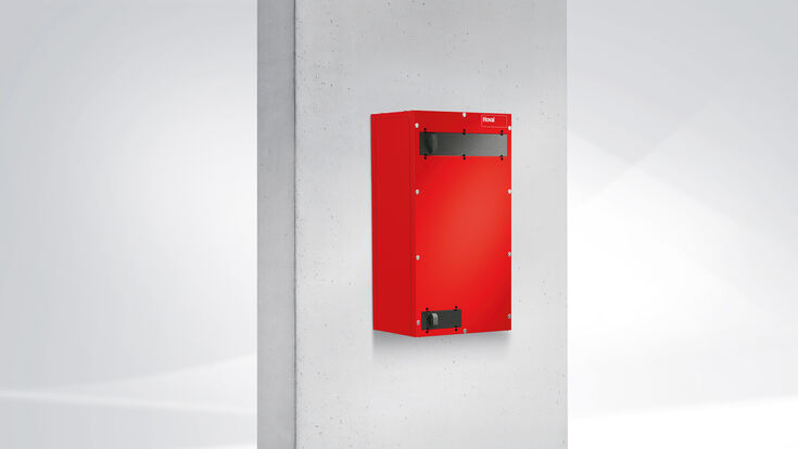 © Hoval Das rote Lüftungsgerät an einer grauen Mauer montiert.
