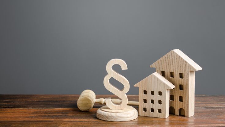 © Andrii Yalanskyi - stock.adobe.com Wooden houses and paragraph figurine with judge hammer. Litigation in housing and real estate disputes. Norms and rules for construction, maintenance. Encouraging green and energy-saving technologies