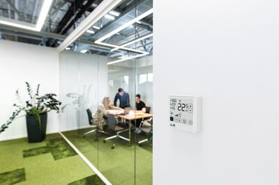© Belimo/René Gaens Konferenzraum mit Menschen im Hintergrund, Raumklimagerät an der Wand im Fokus.