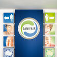 Der Eingang zu einer Sanifair-Toilettenanlage mit einem großen Sanifair-Poster mittig im Bild.