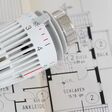 Ein Thermostat-Knauf liegt auf einem Gebäudeplan.