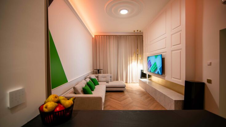 © Loxone Die "Lounge" des Büros: Ein langer Raum mit einem Fenster am Ende und Vertäfelungen auf der rechten Wand. Ein großes Sofa und ein Fernseher sind in der Mitte.