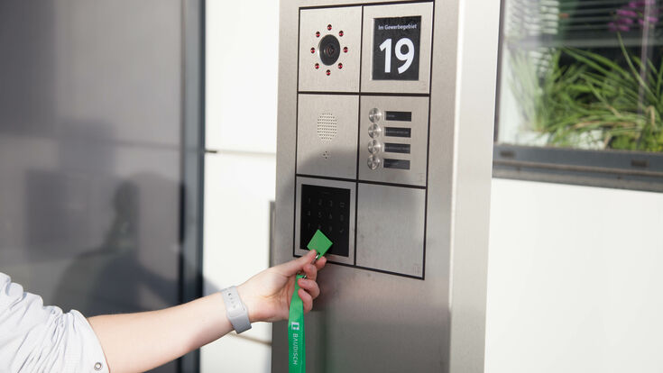 © Loxone/Susan John Eine elektronische Zutrittssicherungsoberfläche an der Hauswand mit einer Hand, die einen Zugangschip davorhält.