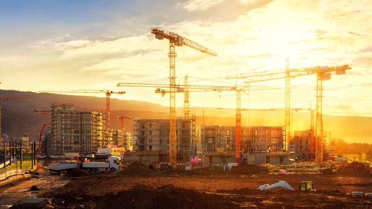 Large construction site including several cranes working on a building complex, illumined by warm gold sunlight
