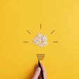 Light bulb of blank puzzle pieces as the bulb and hand drawn neck and rays over yellow background in a conceptual image of vision and idea.