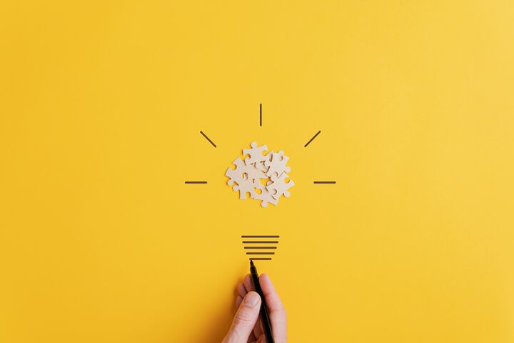 Light bulb of blank puzzle pieces as the bulb and hand drawn neck and rays over yellow background in a conceptual image of vision and idea.