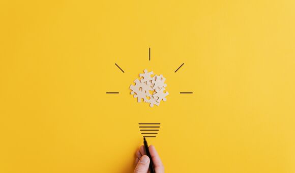 Light bulb of blank puzzle pieces as the bulb and hand drawn neck and rays over yellow background in a conceptual image of vision and idea.