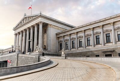 © EdNurg - stock.adobe.com main entrance of Austrian parliament building in Greek style with statues of philosophers and white columns with famous Pallas Athena fountain and in Vienna
