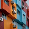 Striking building facade captivates with its bold hues of orange, red, and blue, complemented by air conditioning units, reflecting urban life and architectural creativity.