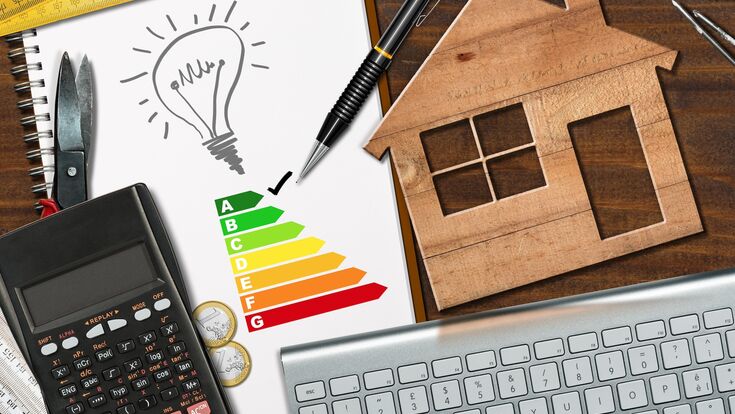 Energy efficiency rating graph on a desk with a wooden house model, calculator, folding ruler, light bulb and a computer keyboard