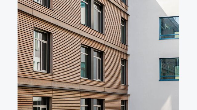 Der großflächige Einsatz von Holz umfasst auch die Fassade des Neubaus. Zur Verhinderung des vertikalen Brandüberschlags wurden auskragende Bleche in die Fassadenlamellen integriert.